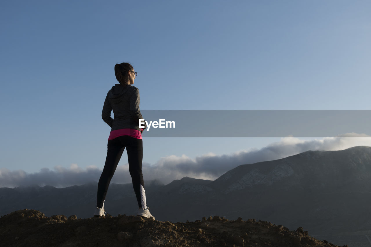 Rear view of woman standing on mountain against sky