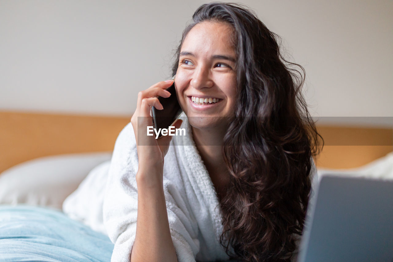 Happy woman speaking with cellphone in bedroom at home