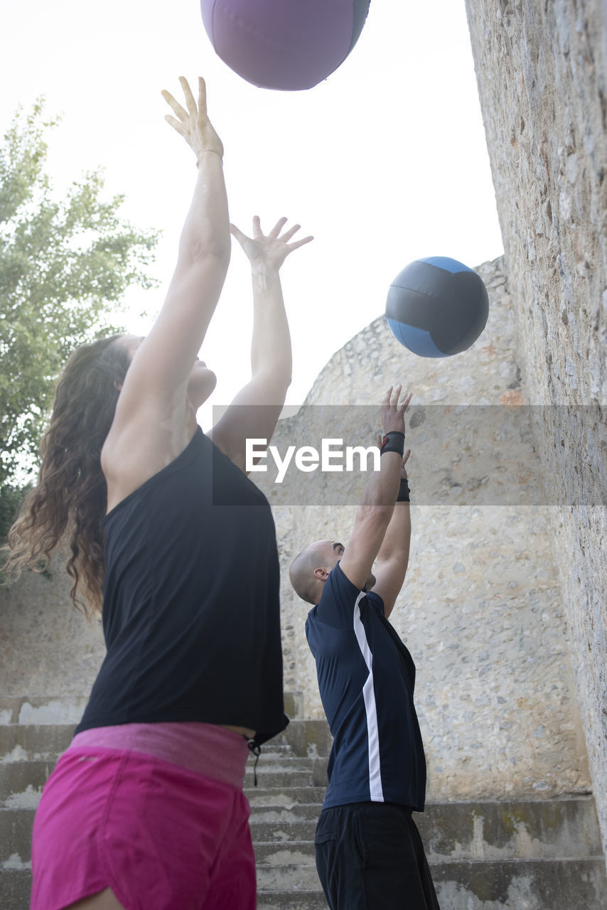 Couple throwing a medicine ball on a wall to practice crossfit.