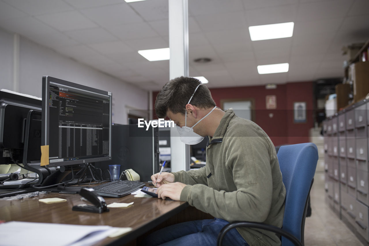 Side view of businessman wearing mask working at desk in office