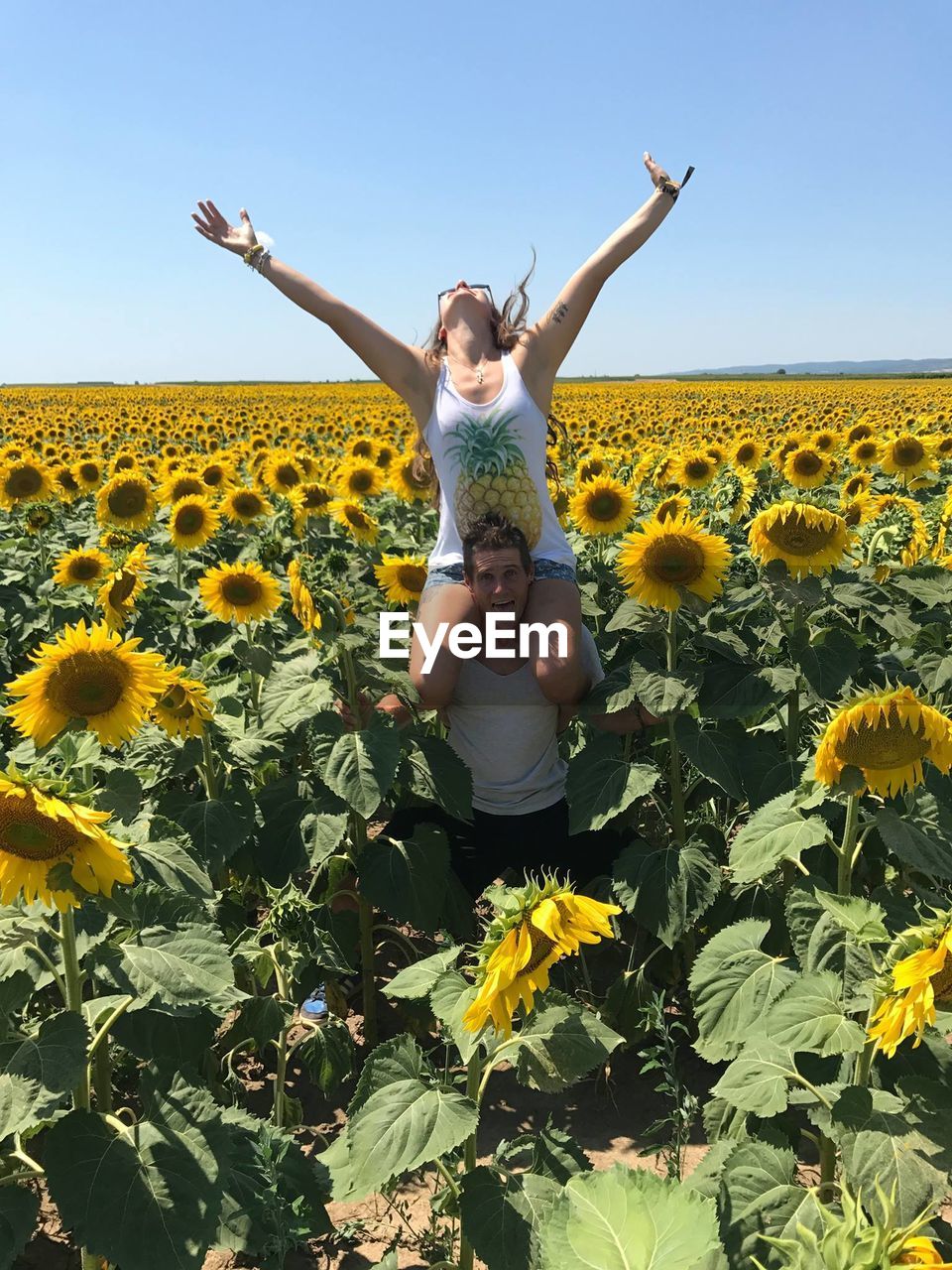 Portrait of boyfriend carrying girlfriend on shoulders at sunflower farm