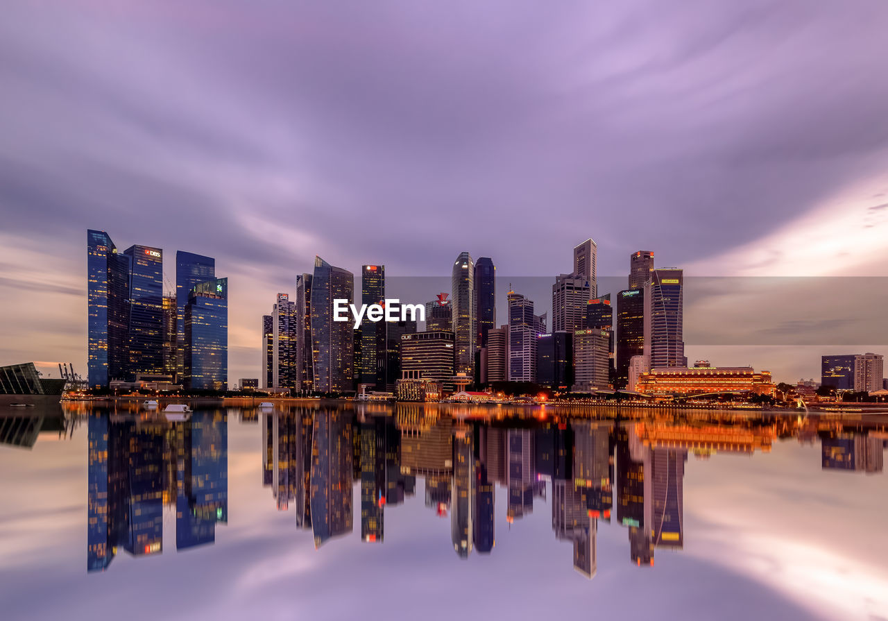 Reflection of illuminated buildings in sea against sky