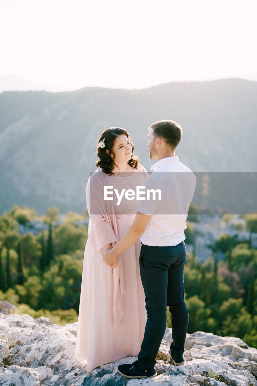 YOUNG COUPLE STANDING ON MOUNTAIN AGAINST SKY