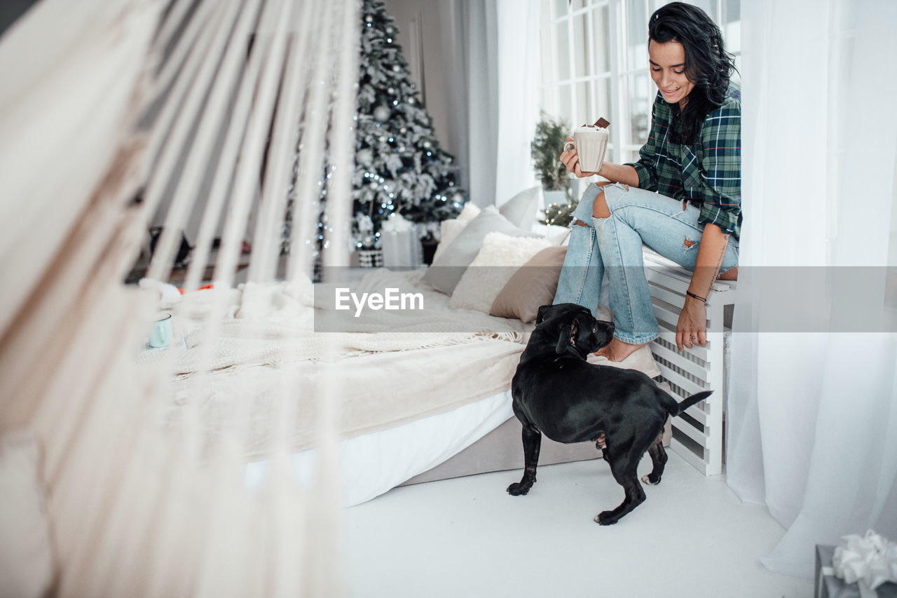 Smiling woman holding hot chocolate while sitting with dog at home