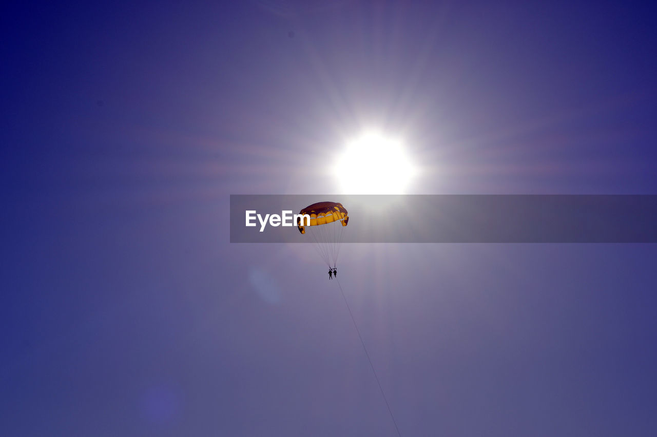 Low angle view of people parasailing against clear sky