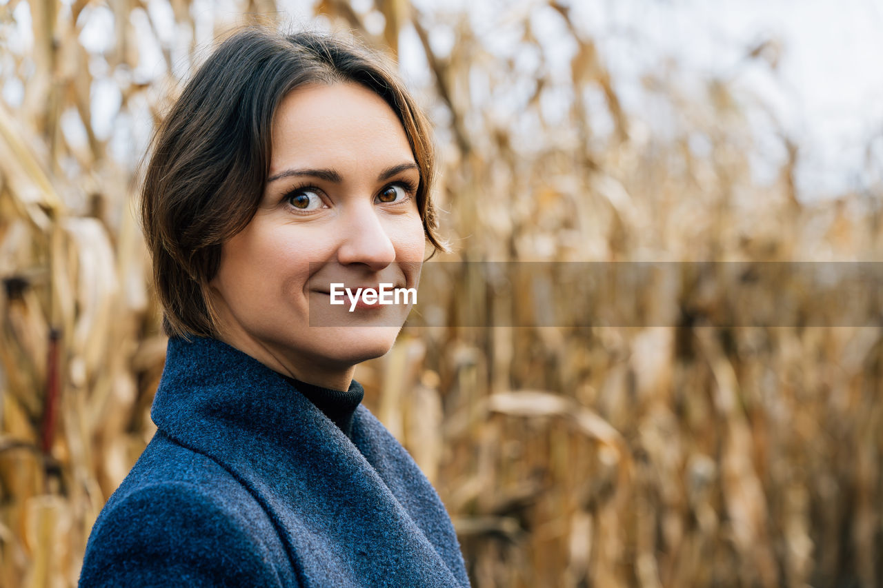 Portrait of attractive young woman in autumn coat in cornfield