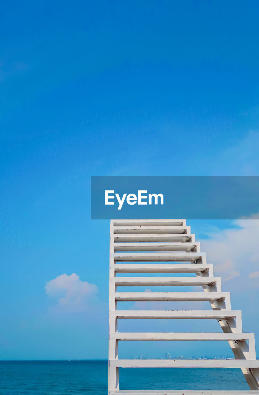 Low angle view of ladder by sea against blue sky