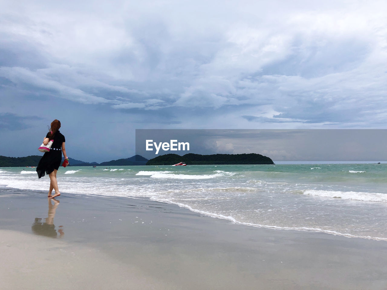 Rear view of woman walking at beach against sky