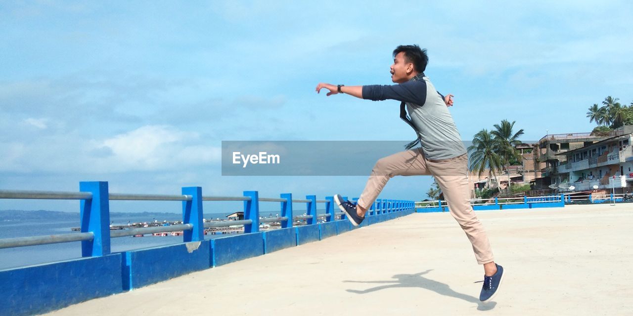 Full length of young man jumping on beach against sky