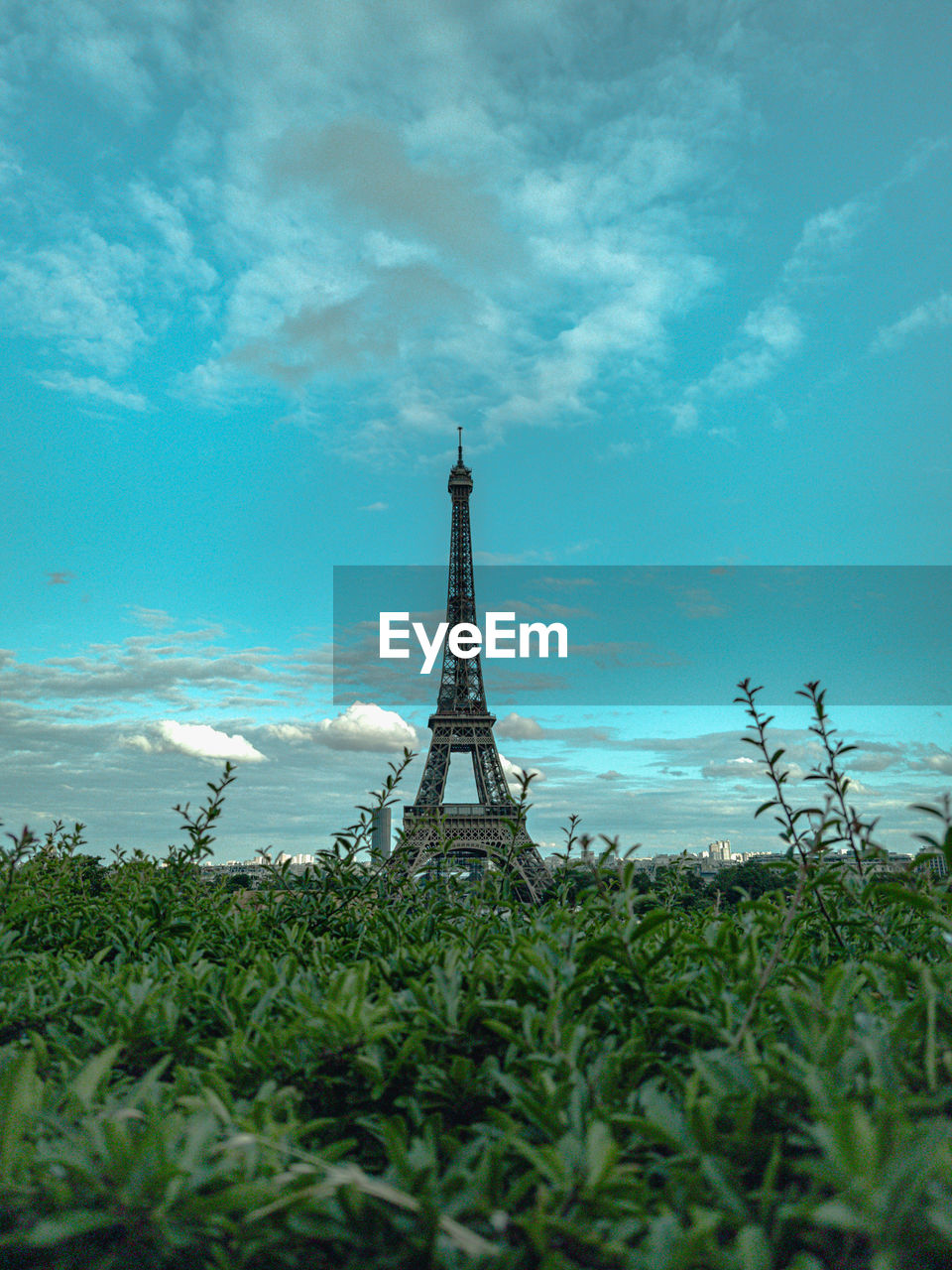 View of eiffel tower on field against cloudy sky