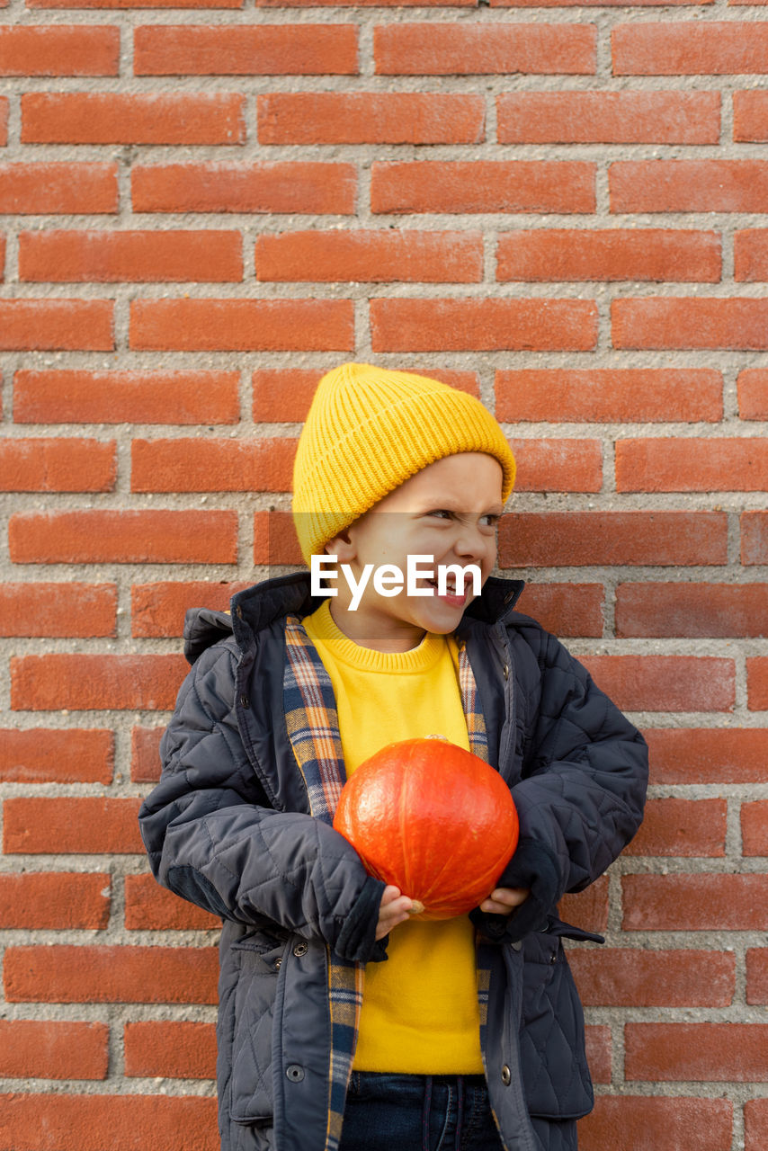 Boy with a pumpkin in his hands against a brick wall.