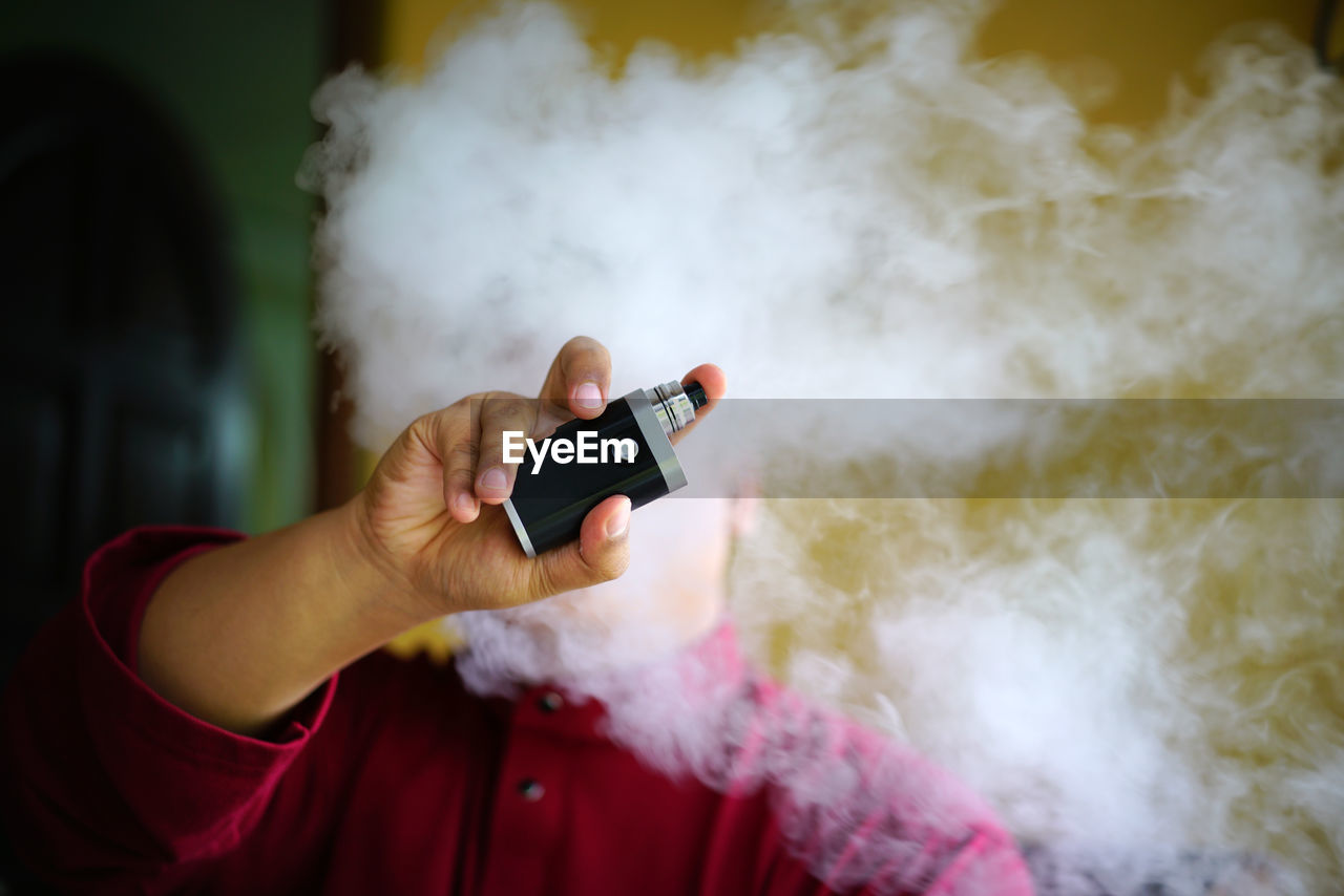 Close-up of man holding electronic cigarette amidst smoke