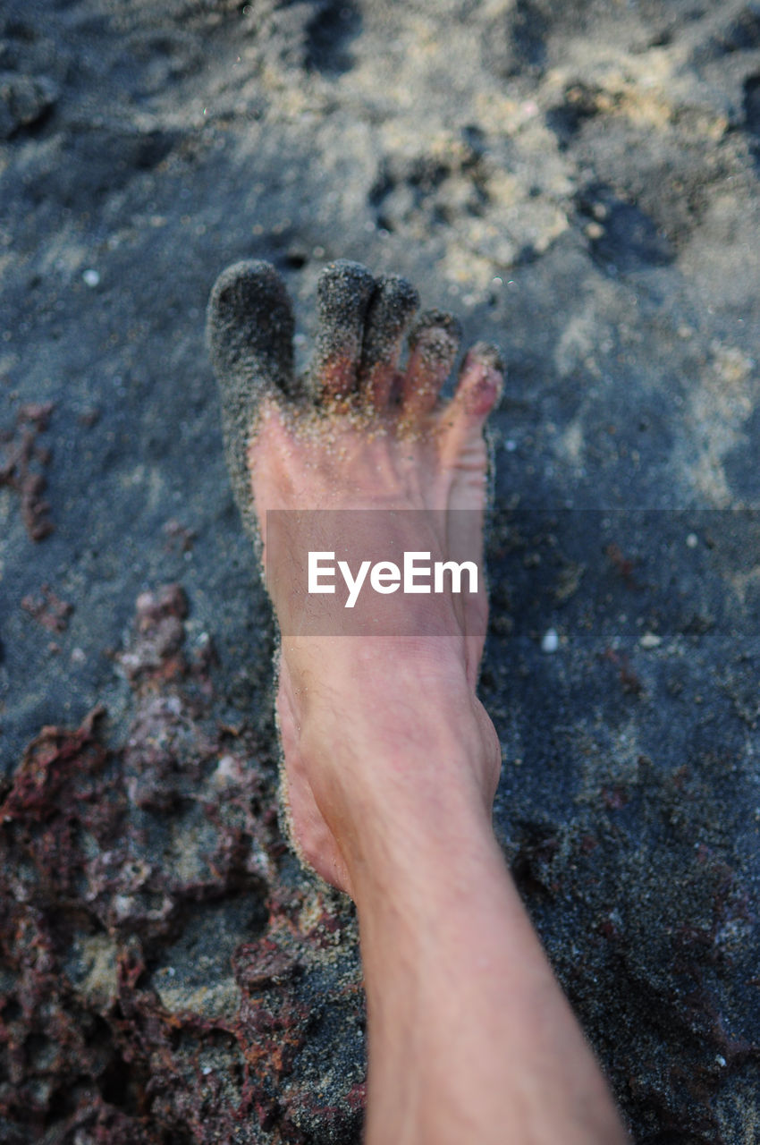 Close-up of messy human foot on sand at beach