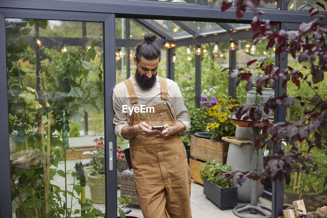 Man using cell phone in front of greenhouse