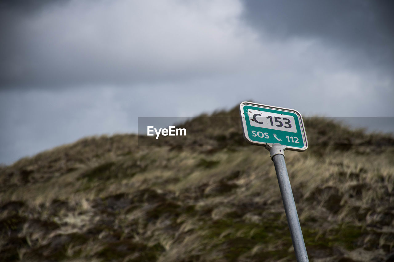 Low angle view of road sign with numbers and alphabets against sky