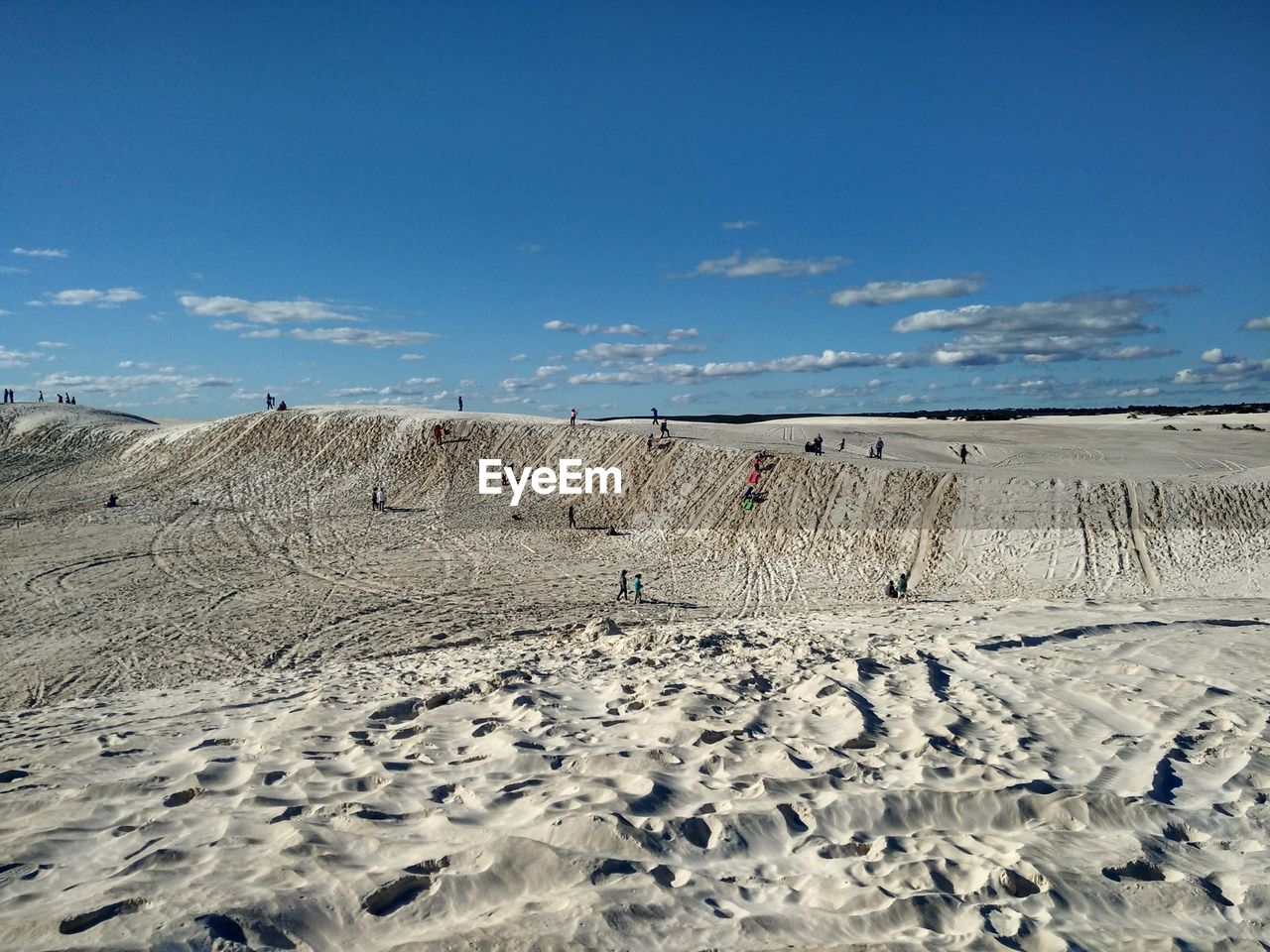 TIRE TRACKS ON SAND DUNE AGAINST BLUE SKY