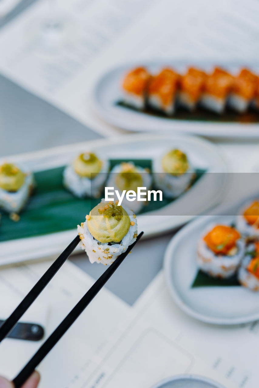 Vertical view of the hands holding wasabi sushi and rolls with wooden chopsticks