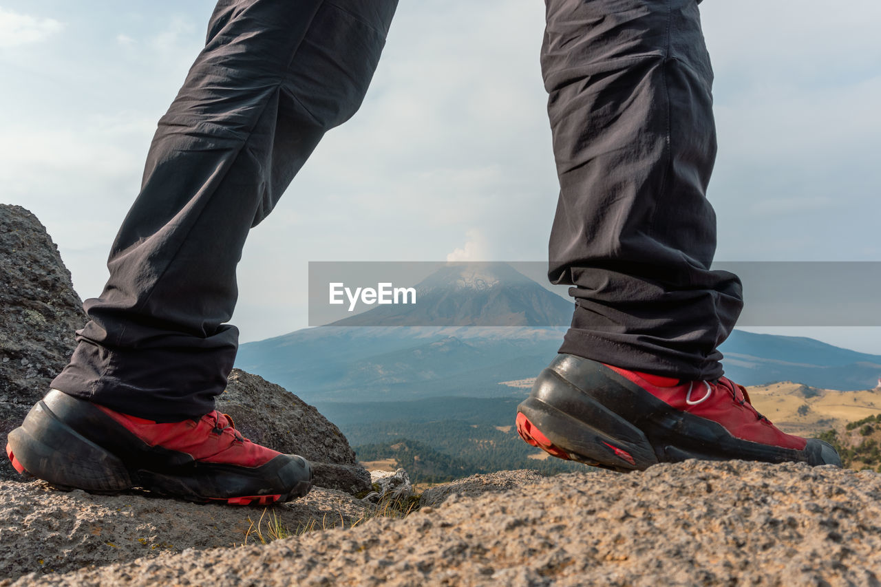 low section of man standing on rock against sky