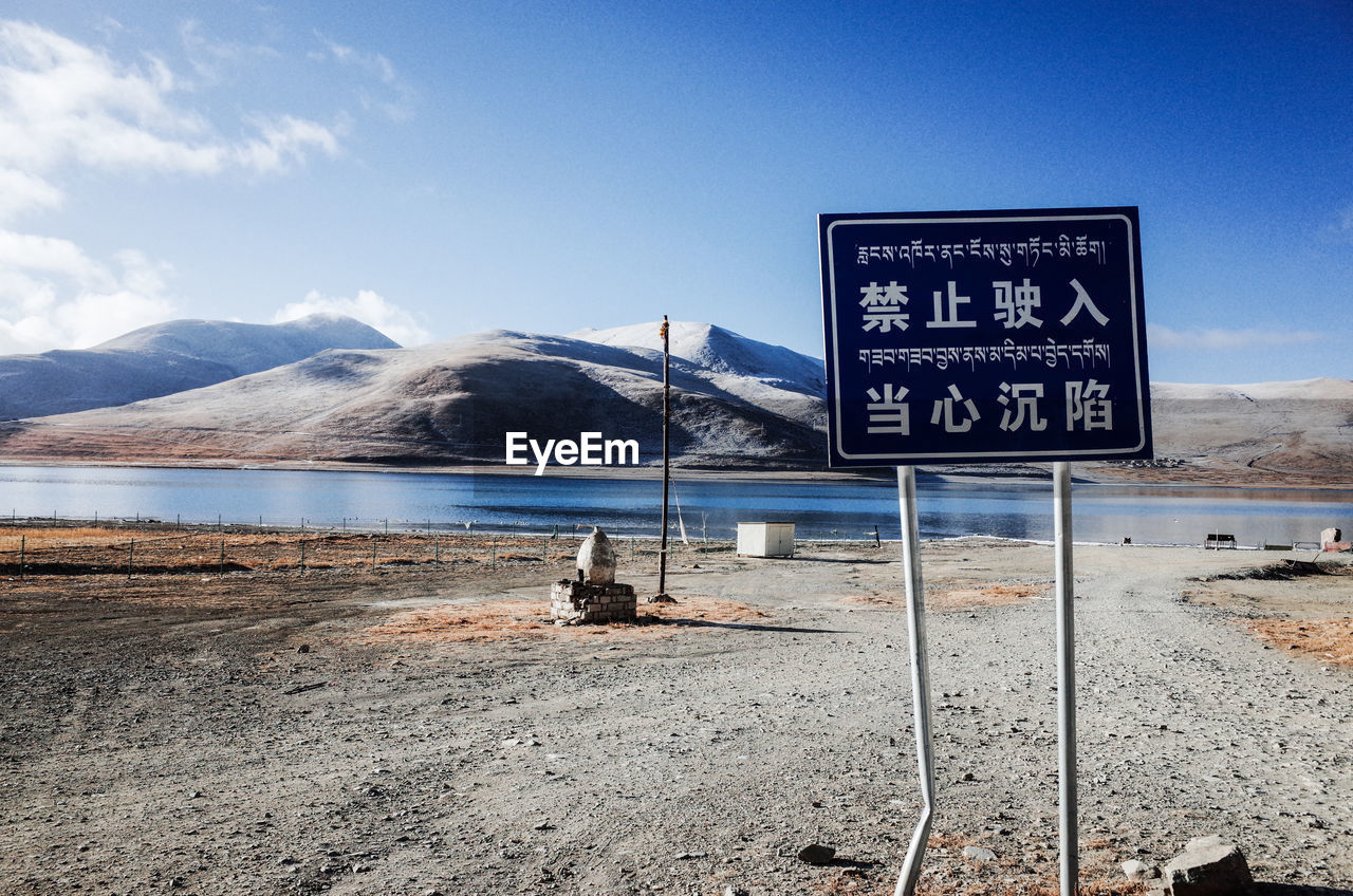 Information sign on road by mountain against sky