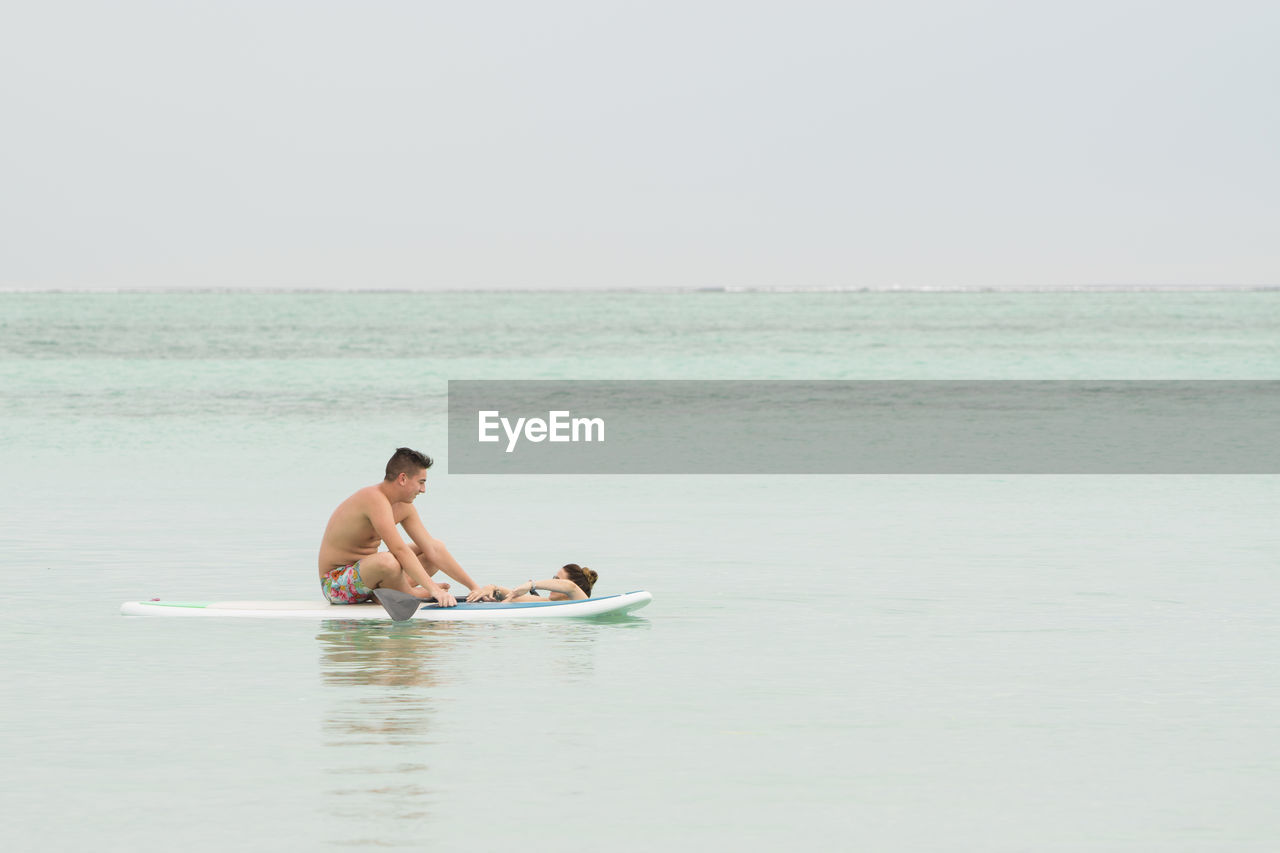 Friends paddleboarding in sea against sky