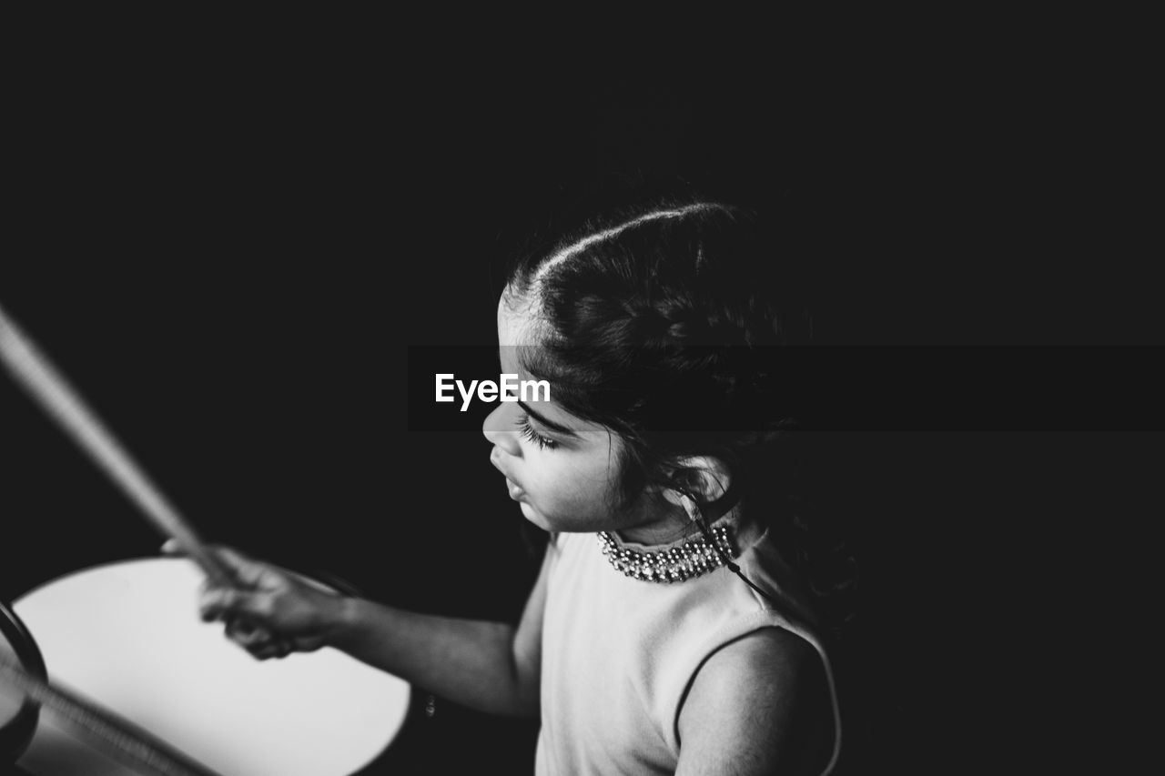 Girl playing musical instrument against black background