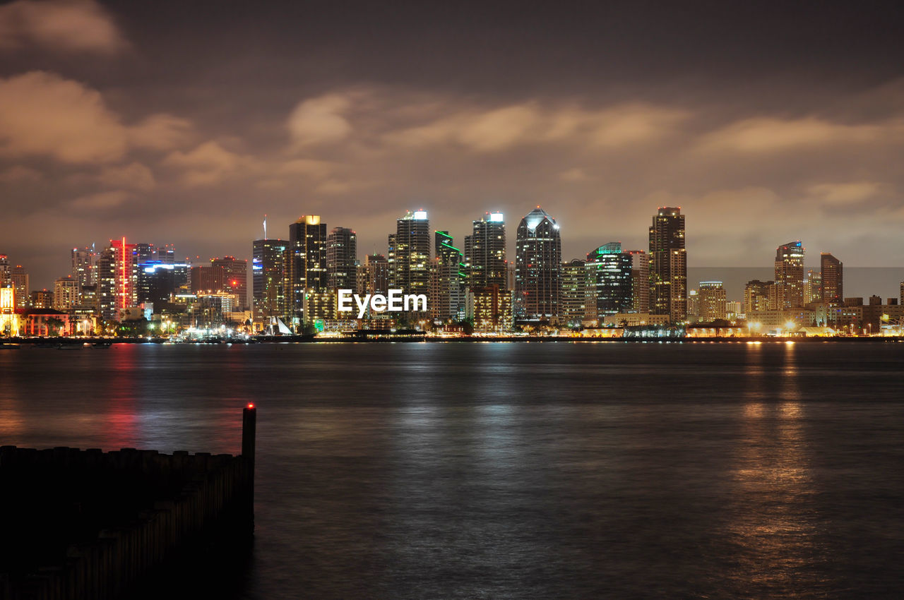 Illuminated city at waterfront against sky during dusk