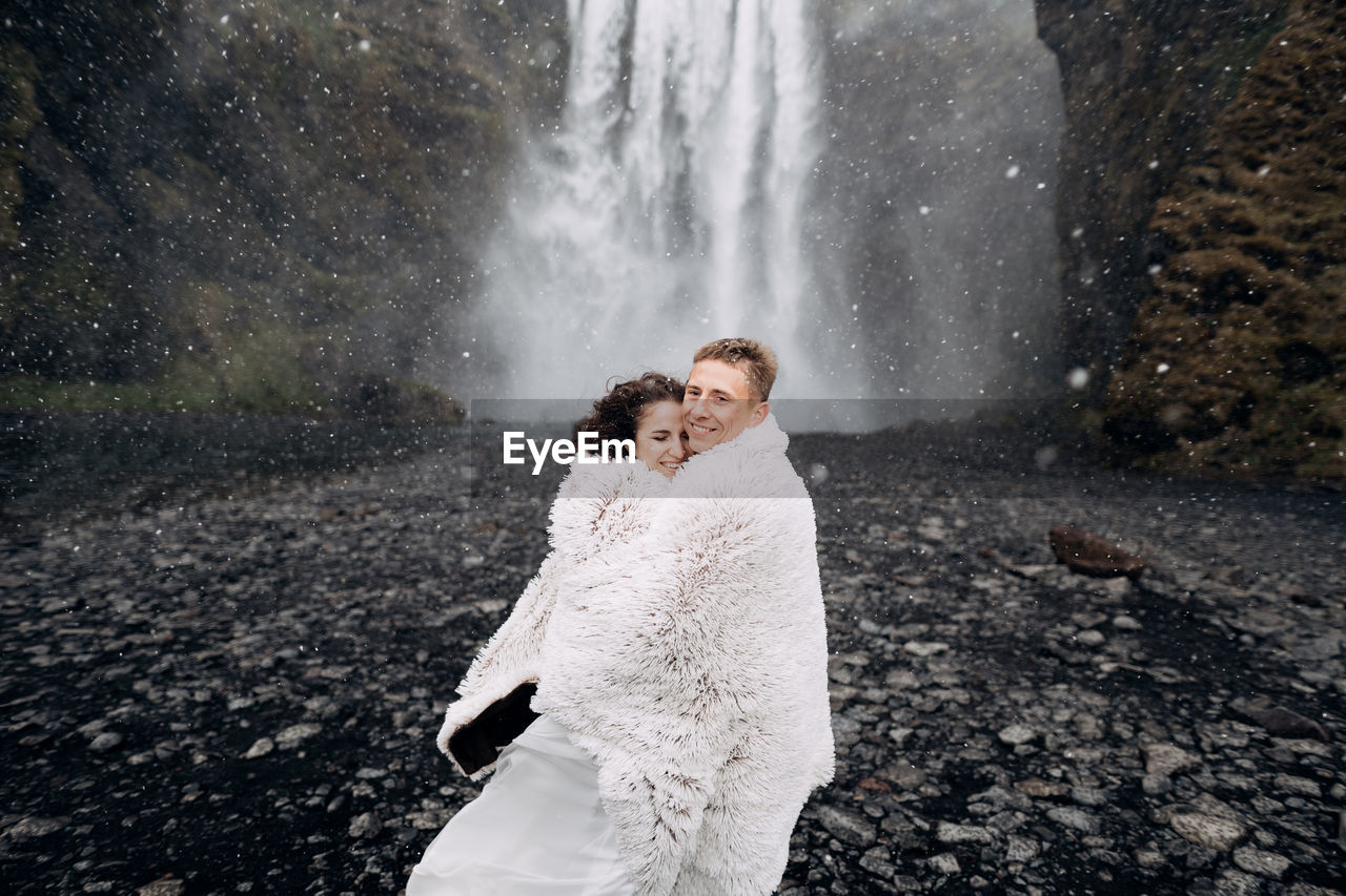 REAR VIEW OF COUPLE STANDING ON WATERFALL