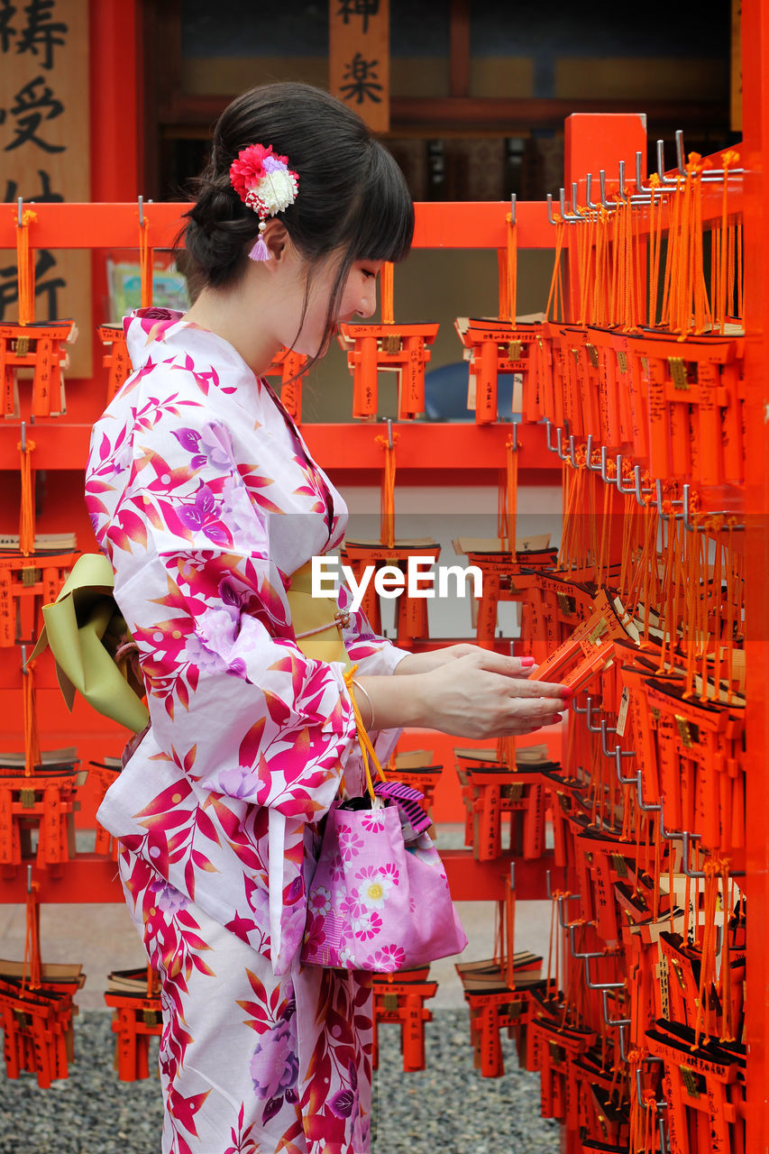 YOUNG WOMAN STANDING IN FRONT OF TRADITIONAL CLOTHING