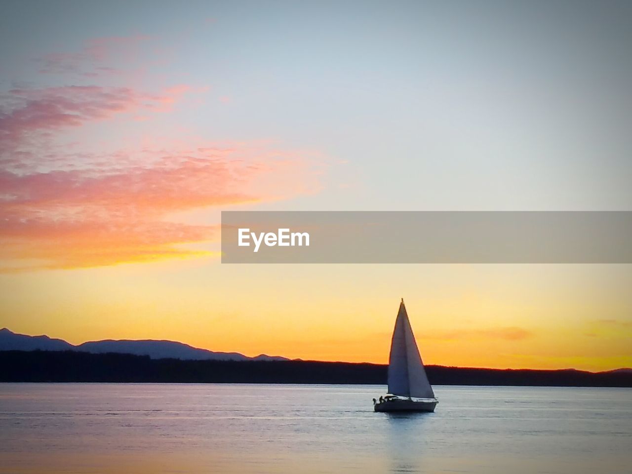 SAILBOAT SAILING IN SEA AT SUNSET