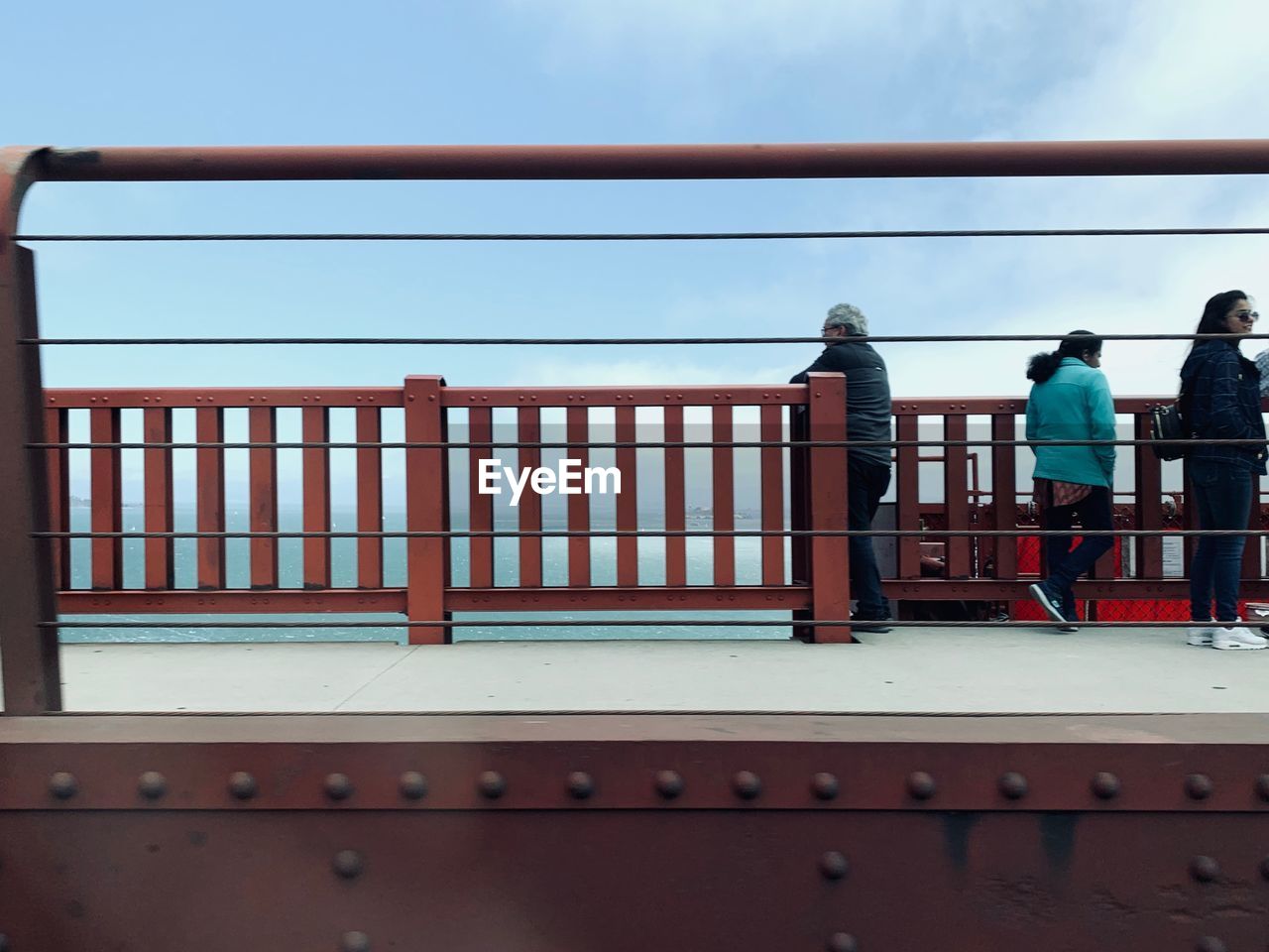 REAR VIEW OF PEOPLE STANDING AGAINST RAILING