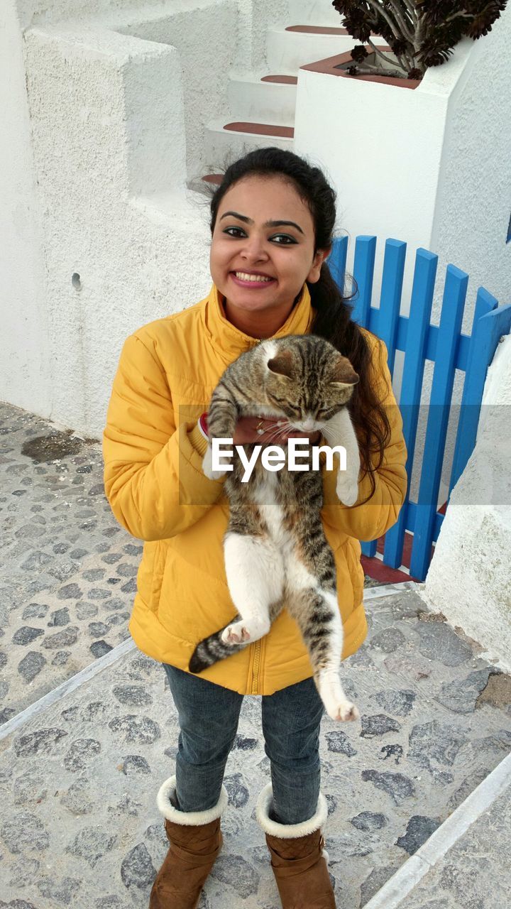 Portrait of smiling young woman holding cat while standing outdoors