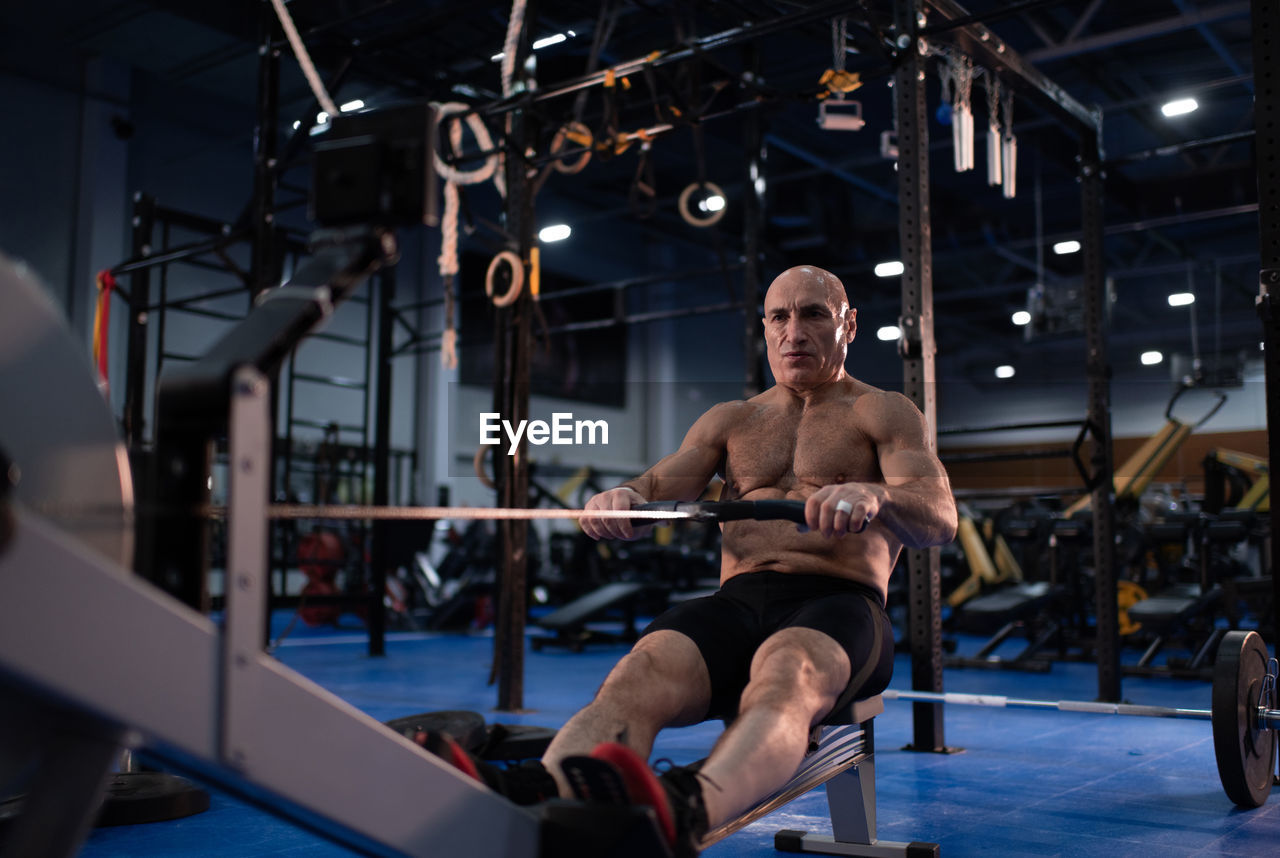 Powerful aged man exercising on rowing machine