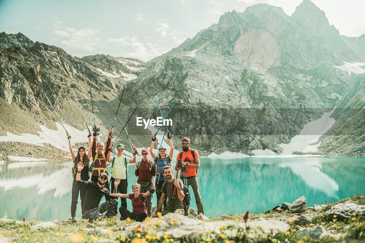 PEOPLE STANDING ON LAKE AGAINST MOUNTAINS