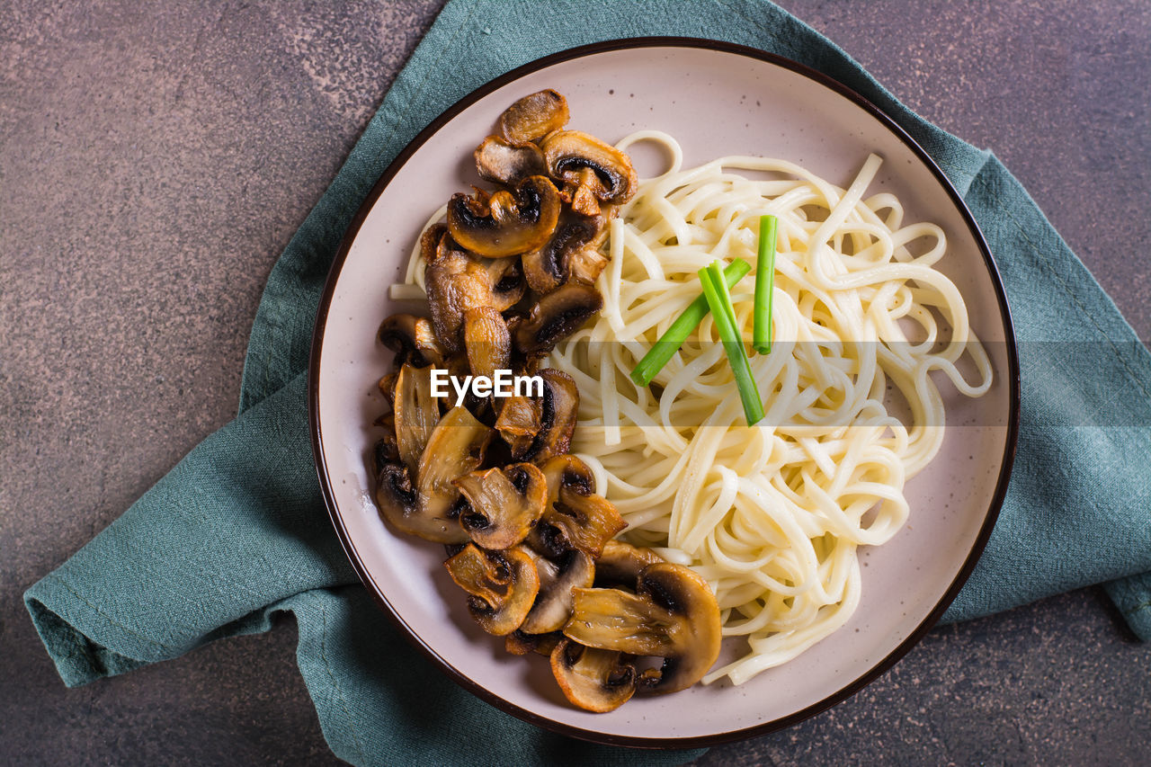 Close up of udon noodles and fried mushrooms on a plate for homemade dinner top view