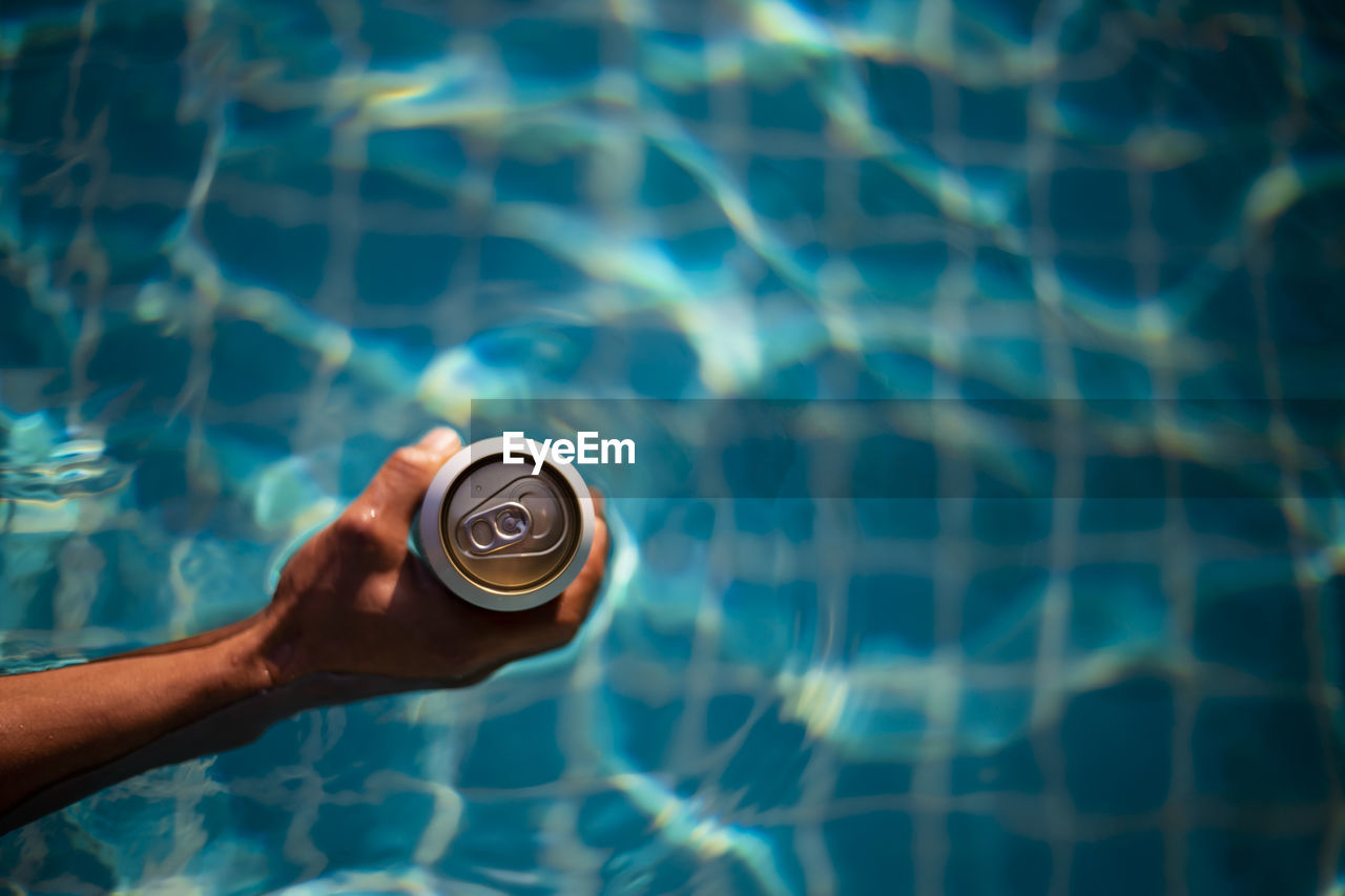 Selective focus white beer can in hand. man is soaking in the pool with an open beer