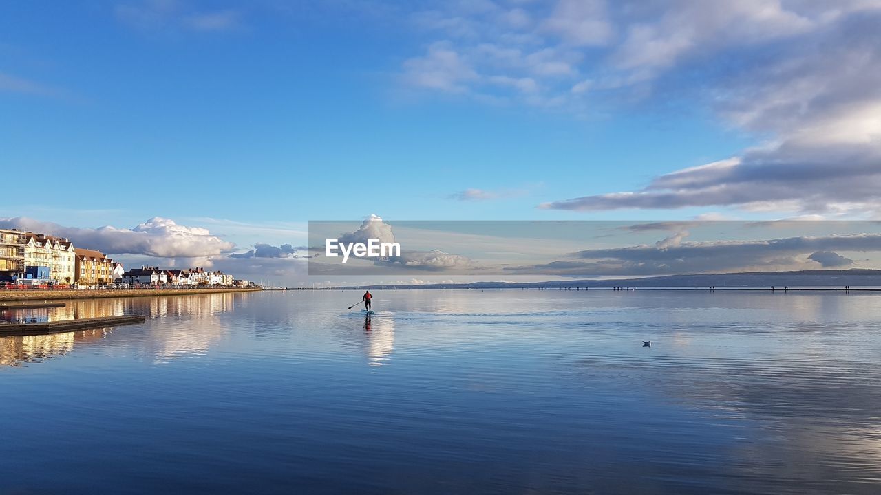 Mid distance of man paddleboarding on sea against cloudy sky