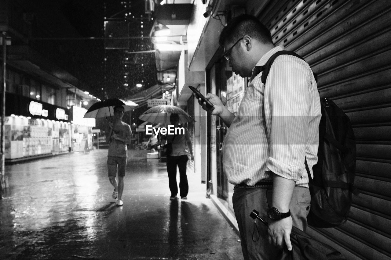 MAN STANDING ON WET ROAD IN CITY