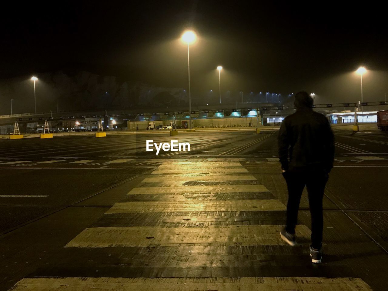 REAR VIEW OF MAN WALKING ON ILLUMINATED STREET LIGHT AT NIGHT