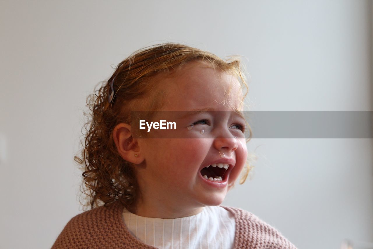 Close-up of girl crying against white background