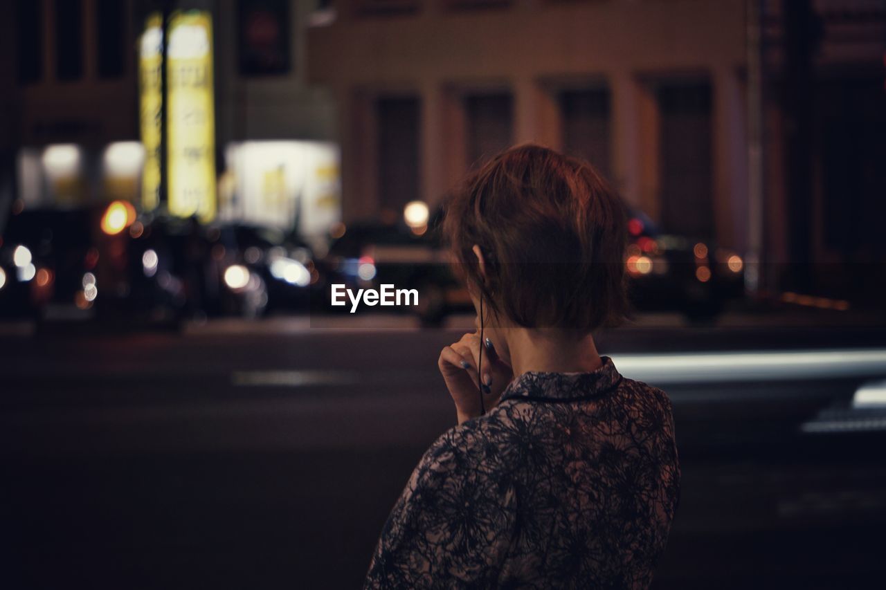 REAR VIEW OF MAN STANDING ON STREET AT NIGHT