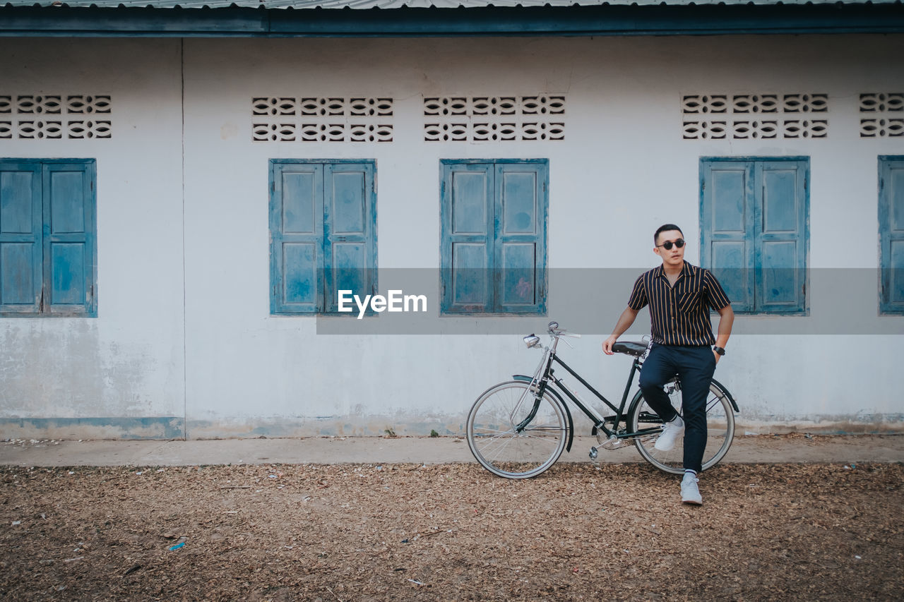 Full length of man sitting outside house on bicycle