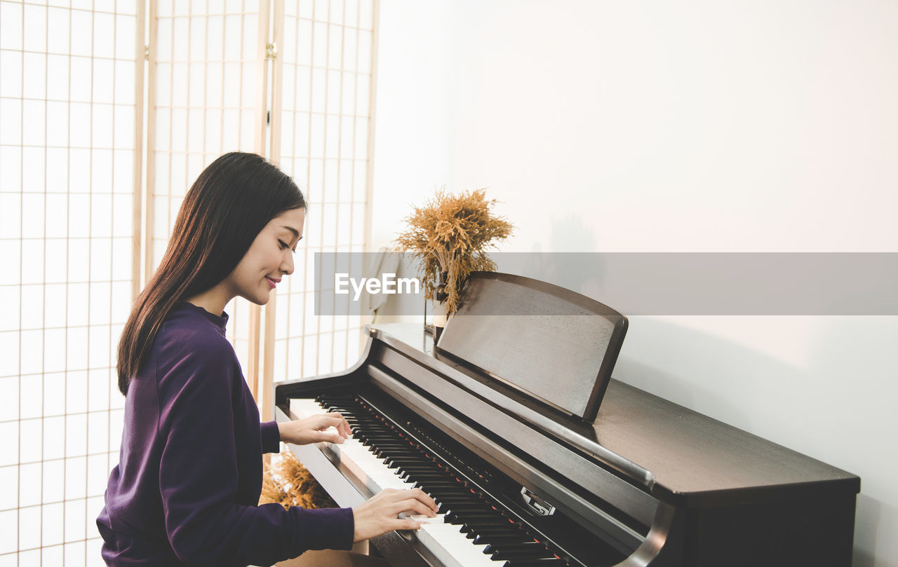 Side view of smiling woman playing piano at home