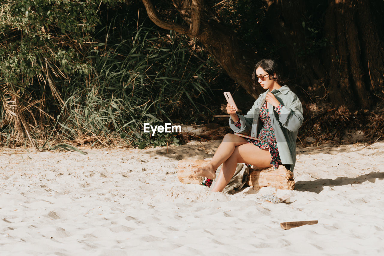 full length of young woman sitting on sand at beach