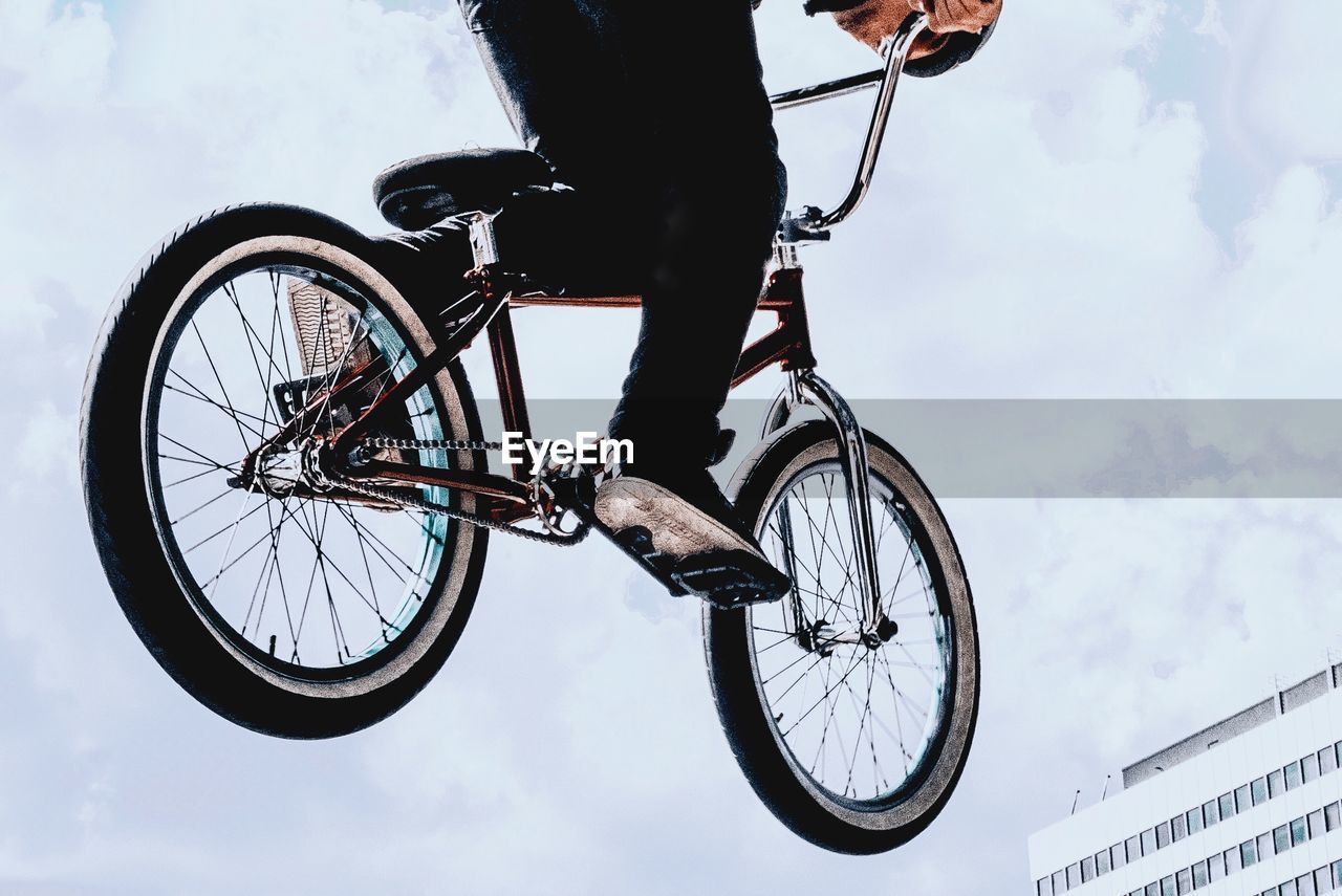 Low section of man riding bicycle against sky