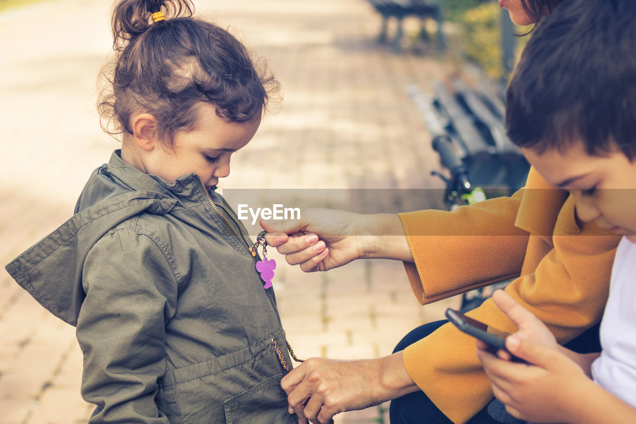 Midsection of mother closing zip of daughter jacket with son at park