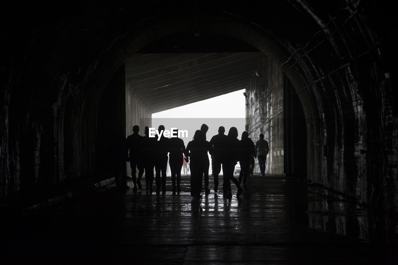 Rear view of silhouette people walking in tunnel