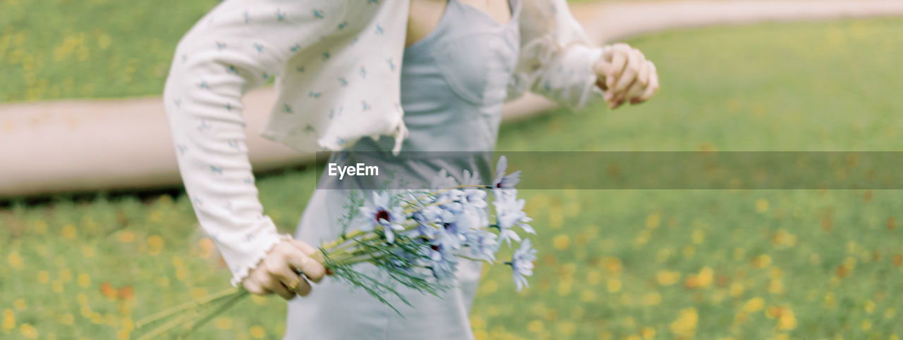 plant, flower, flowering plant, one person, adult, nature, women, field, grass, midsection, freshness, day, focus on foreground, standing, outdoors, beauty in nature, growth, spring, rural scene, young adult, holding, land, yellow, positive emotion, meadow, landscape, emotion, female, lifestyles, clothing, white, fragility, agriculture, leisure activity, limb, flower arrangement, human limb, summer, plain, springtime, close-up, casual clothing, hand
