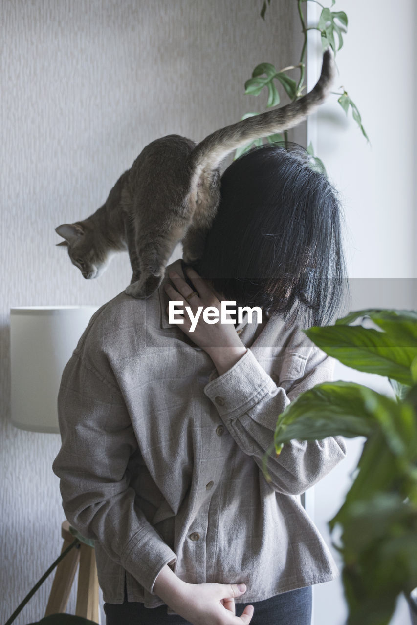 indoors, one person, women, adult, animal, cat, clothing, animal themes, female, green, nature, home interior, casual clothing, lifestyles, three quarter length, person, emotion, plant, waist up, leaf, mammal, plant part, holding, young adult, hairstyle, domestic room