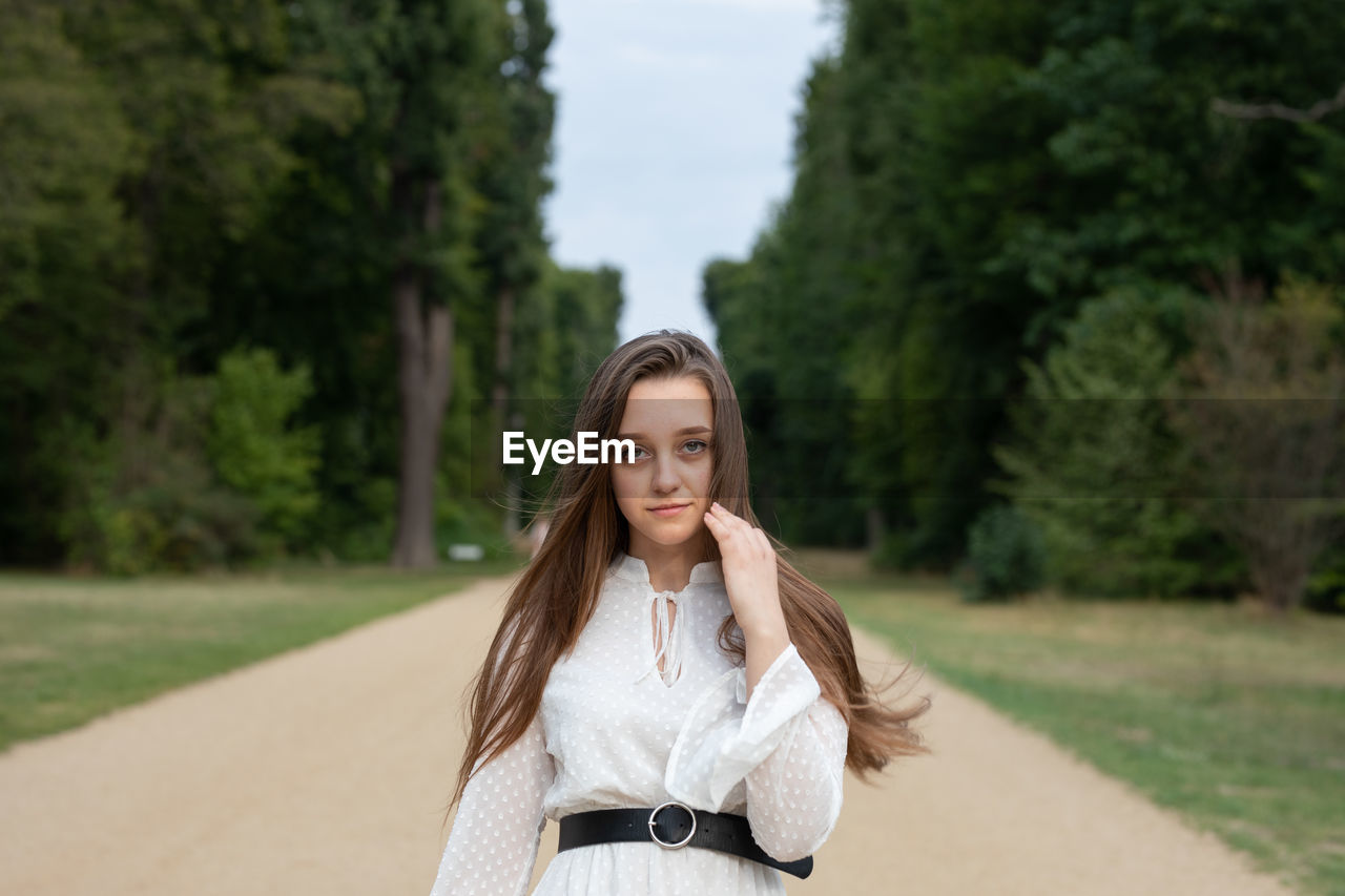 Portrait of beautiful young woman standing against trees