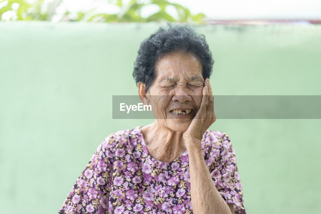 Senior black-haired woman touching the mouth with hand with painful expression because of toothache